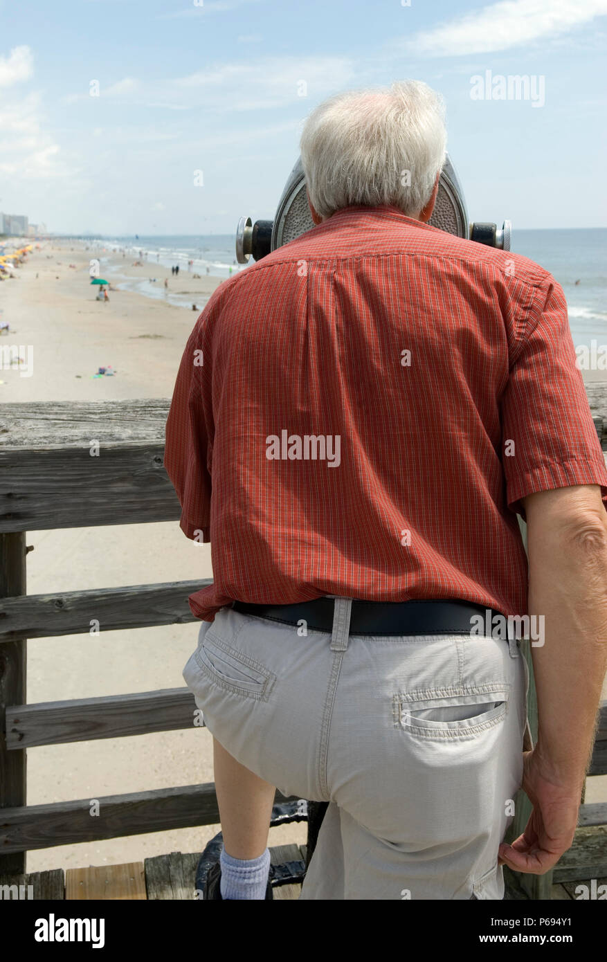 Man looks through binoculars on pier at Myrtle Beach State Park, SC, USA. Stock Photo