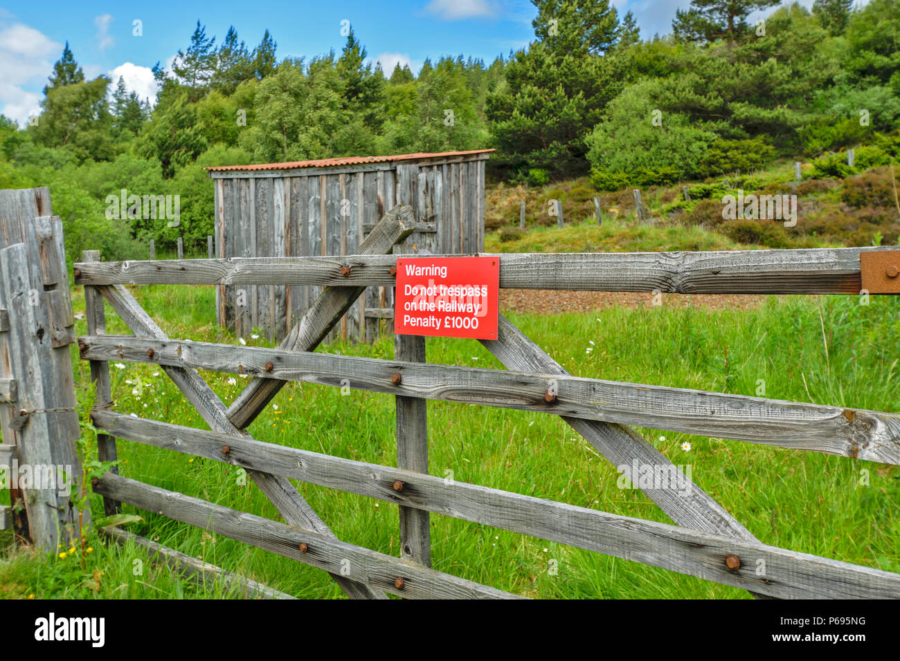 WOODEN GATE OPENING ONTO A RAILWAY LINE WITH WARNING SIGN IN RED DO NOT TRESPASS PENALTY £1000 Stock Photo