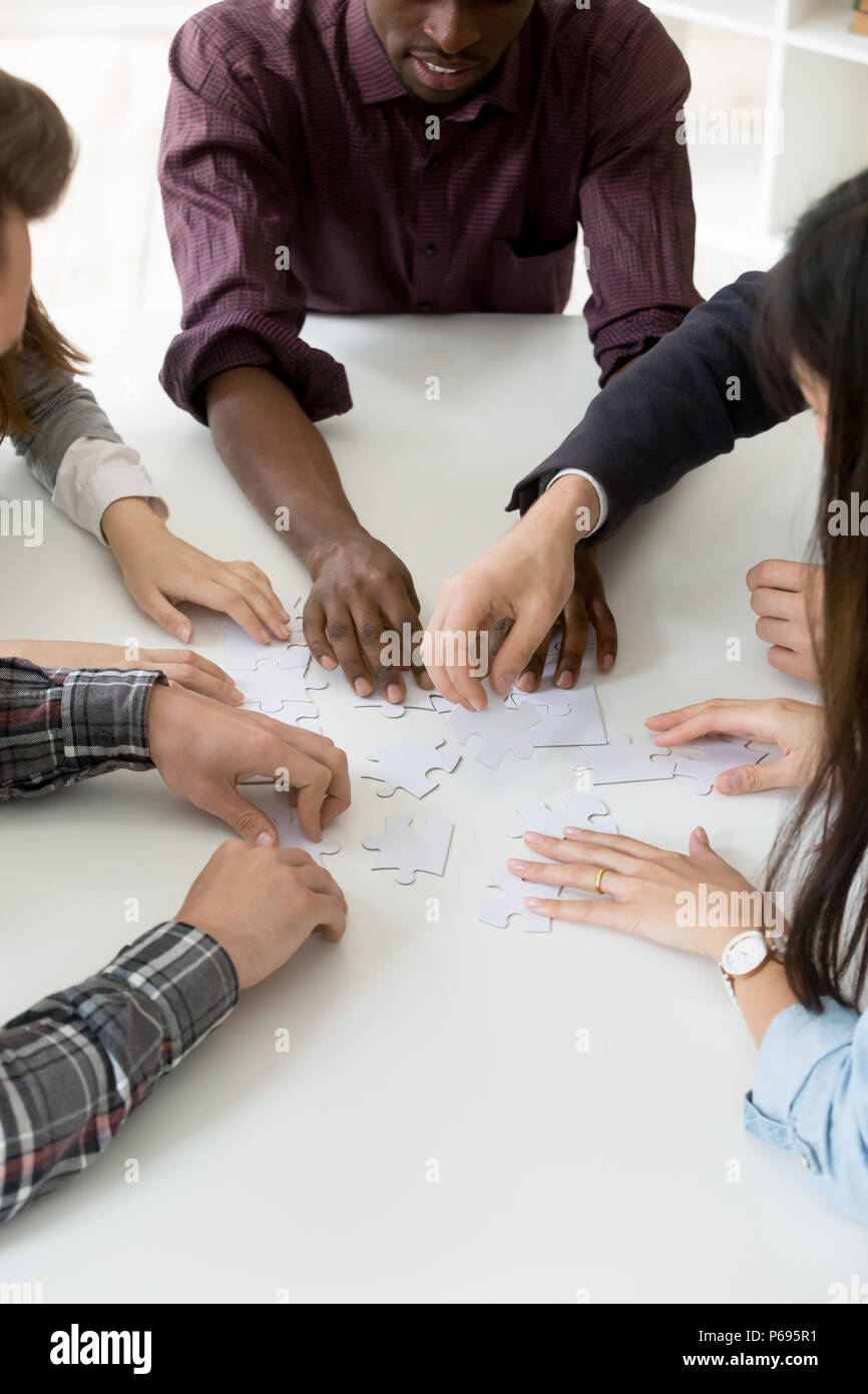 Multiethnic workers assembling jigsaw puzzle while teambuilding Stock Photo