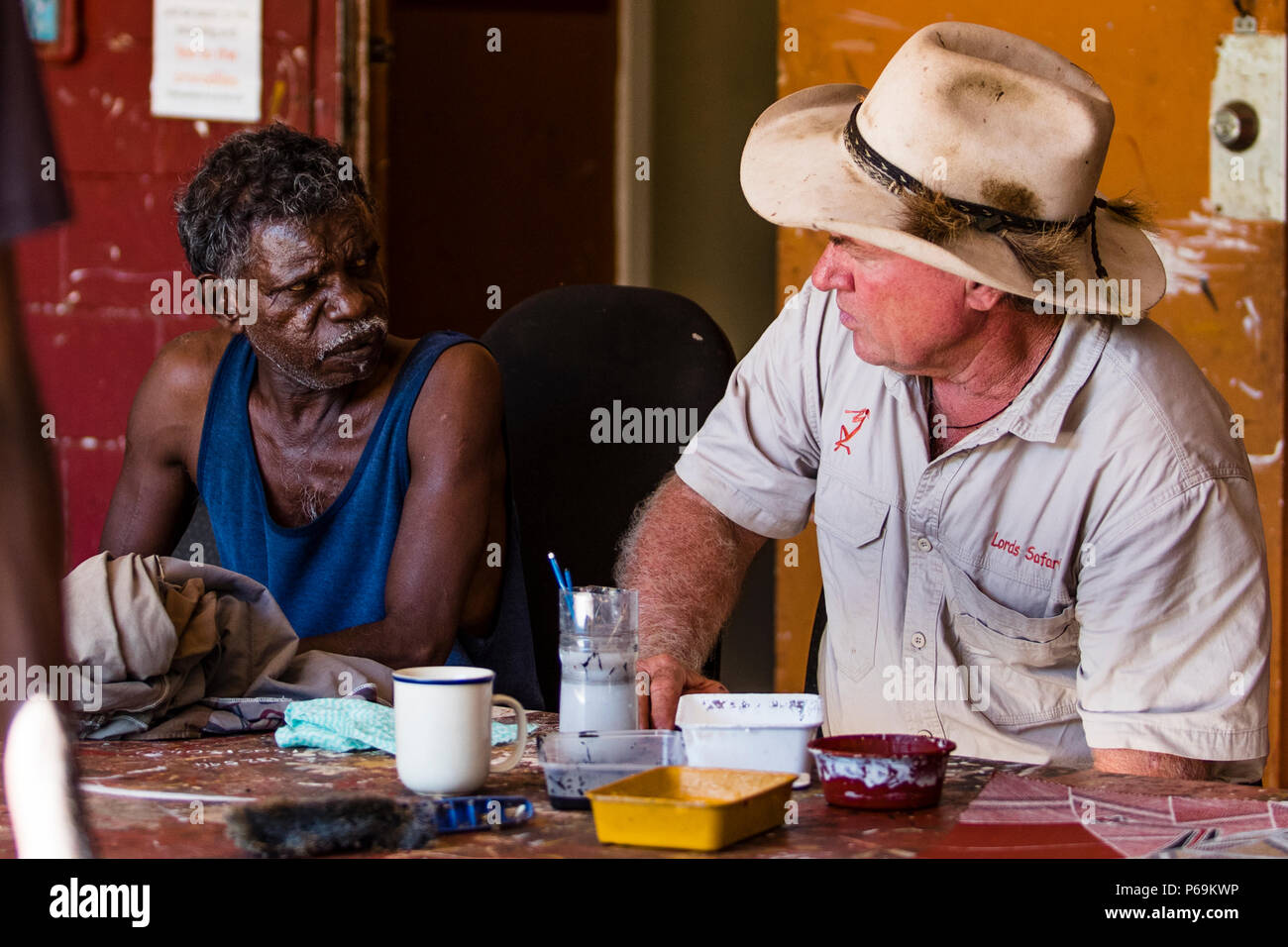 Gabriel, a community decision-maker from Gunbalanya, talks with guide Sab Lord at Injalak Arts in Gunbalanya, Northern Territory, Australia, both seated at a table covered with paint pots. Stock Photo