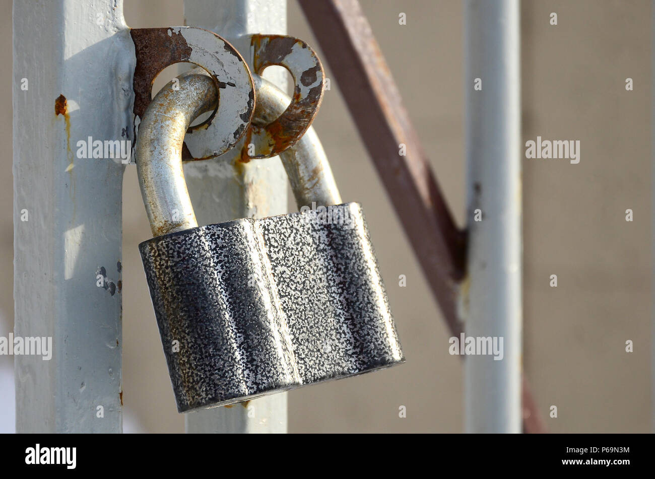 A large gray padlock hangs on a metal gate . Stock Photo