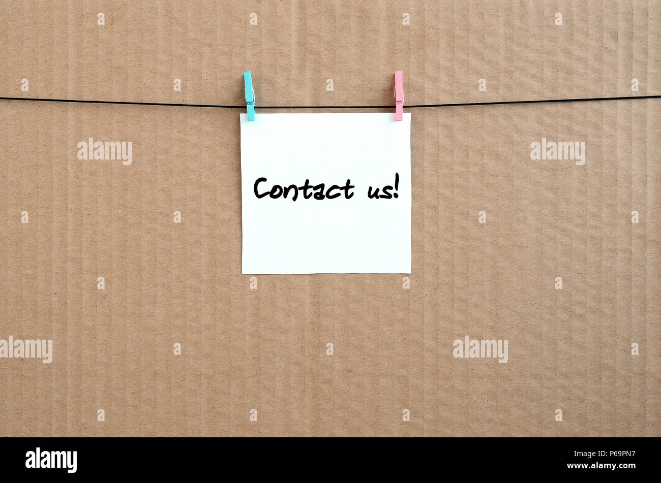 Contact us! Note is written on a white sticker that hangs with a clothespin on a rope on a background of brown cardboard . Stock Photo
