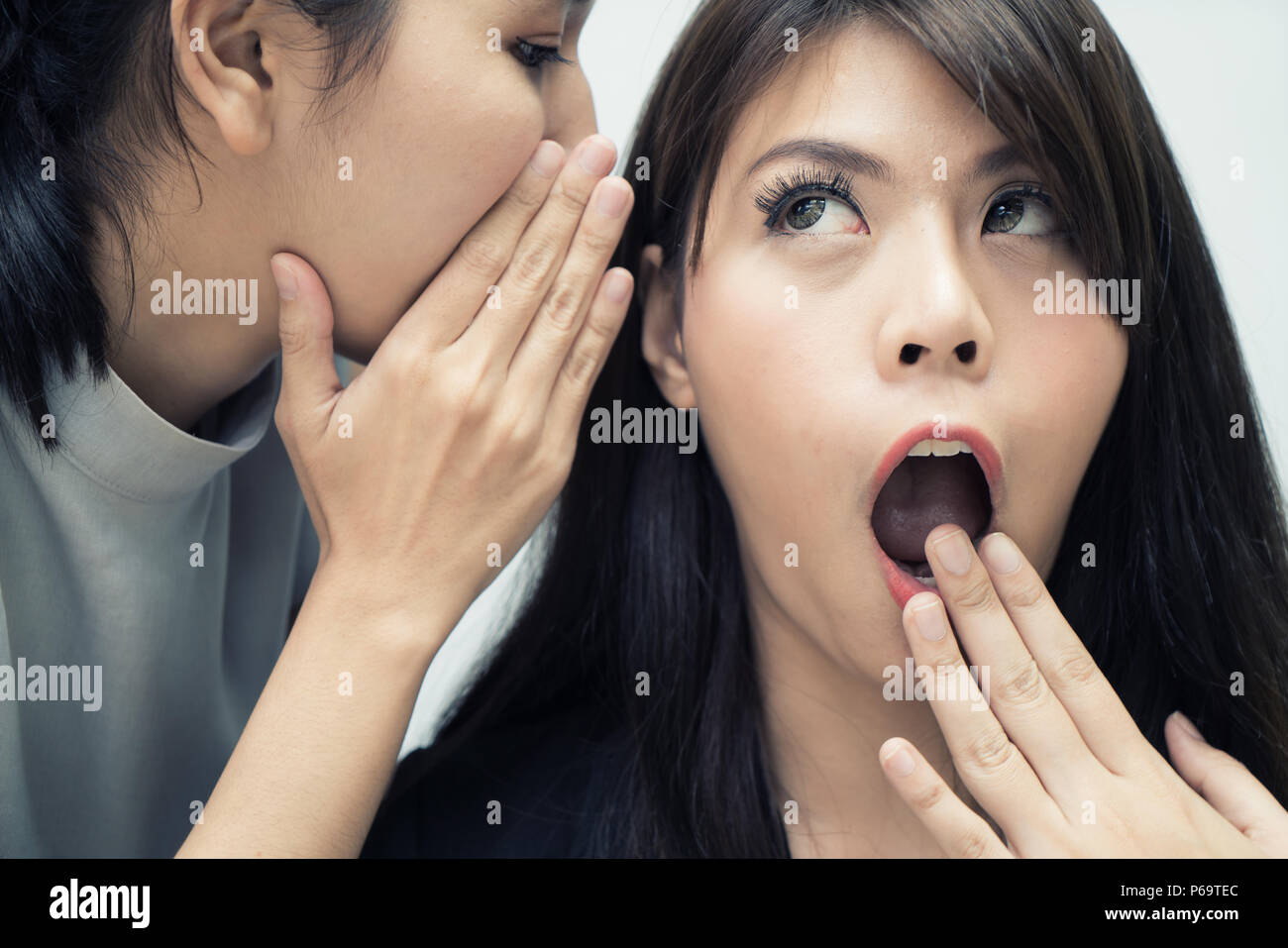Two Asian woman gossip revealing secret to her friend in office. People communication and friendship concept Stock Photo