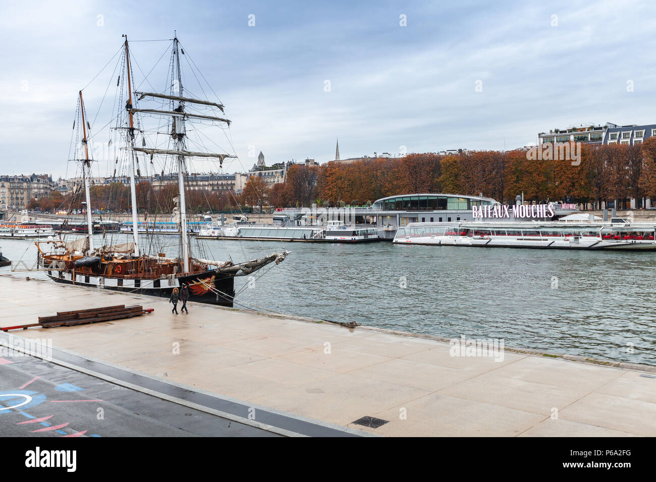 Paris, France - November 4, 2016: Embankments of Paris with moored sailing ship and pleasure boats, ordinary people walk on quayside Stock Photo