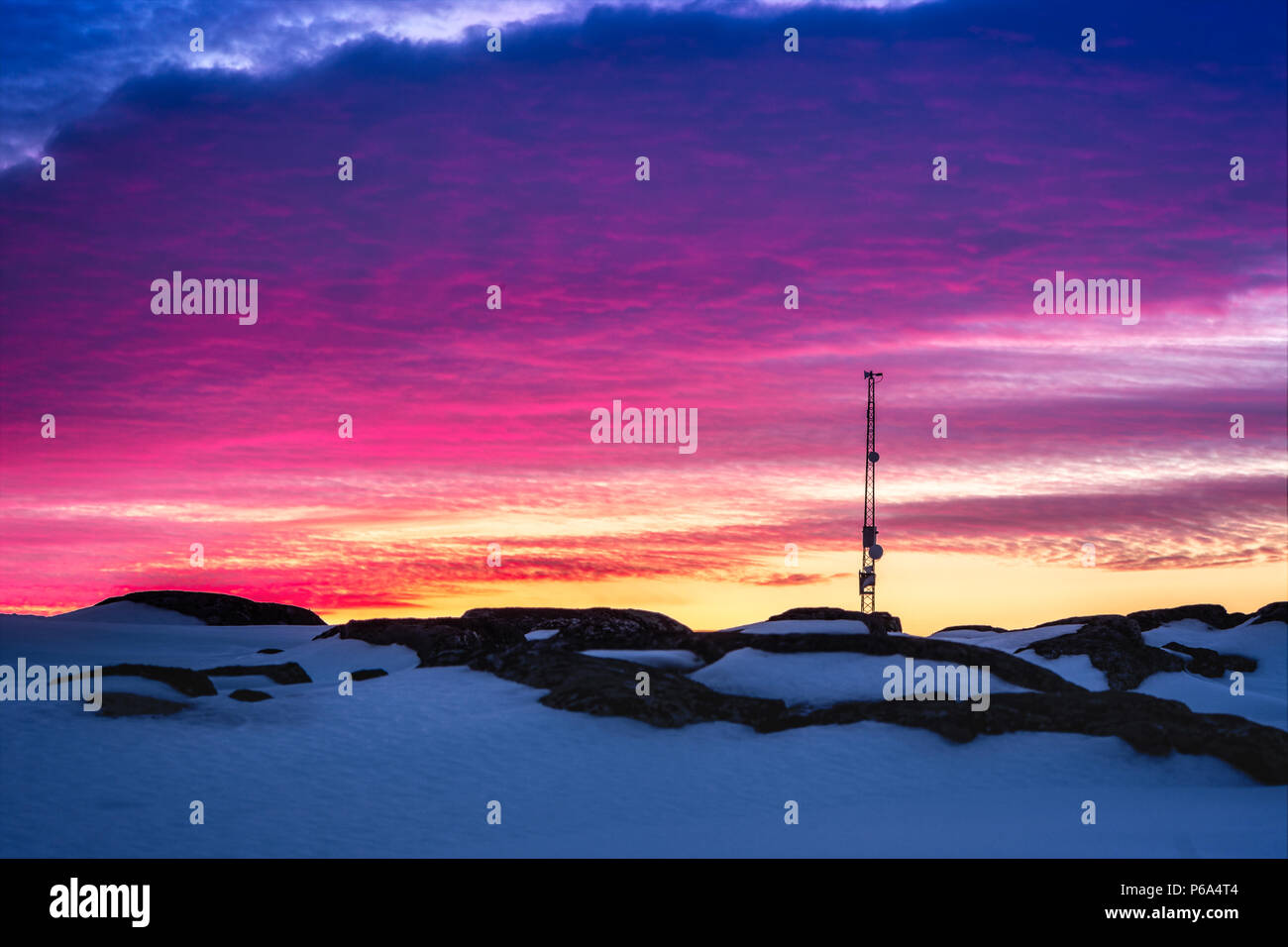 Greenlandic sunset sky with antenna and rocks with snow in the foreground, Nuuk, Greenland Stock Photo