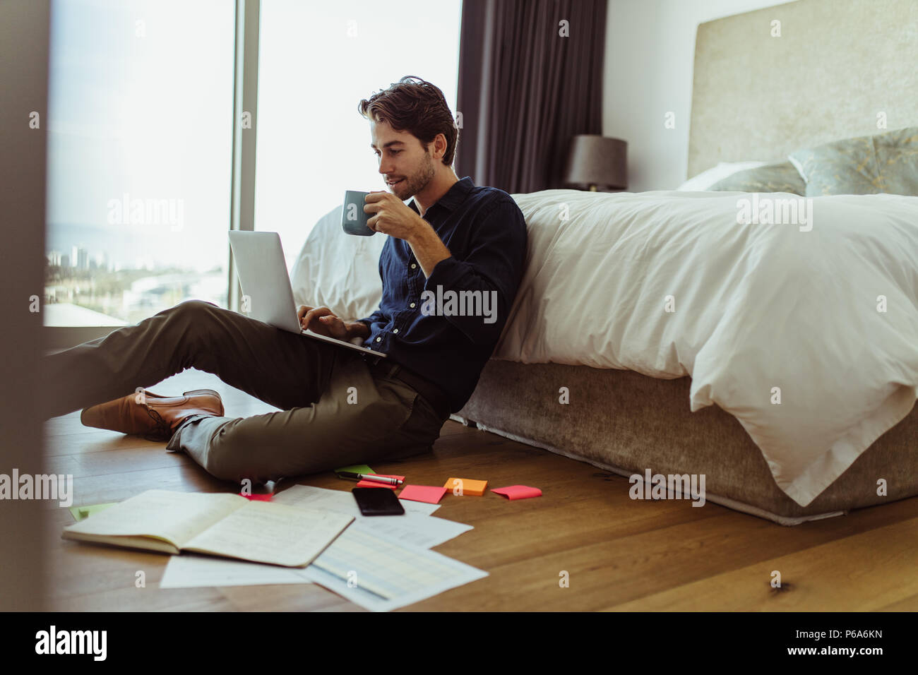 businessman working on laptop computer sitting at home while drinking coffee. Man working on laptop computer sitting on the floor with his diary and o Stock Photo