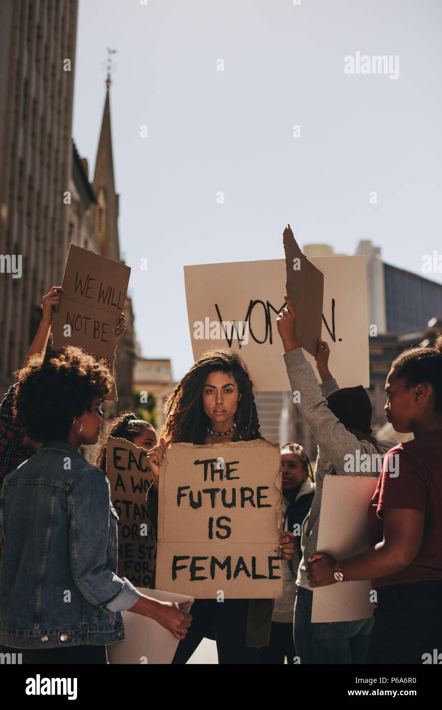 Woman holding a protest sign about women empowerment. Group of women marching on the road in protest. Stock Photo