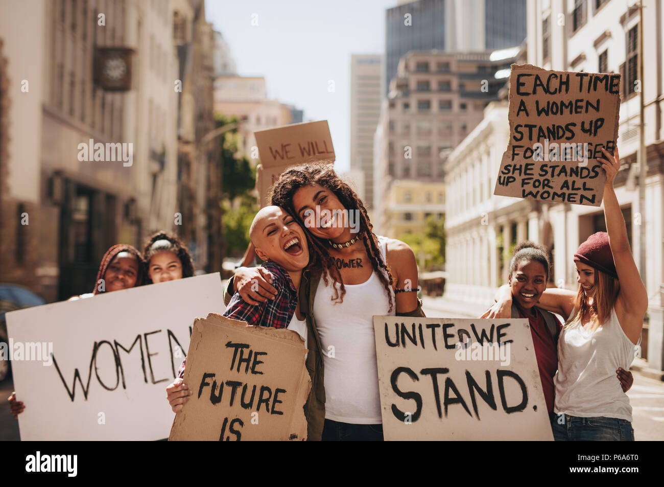 Young women holding banners and laughing during women march. Group of female demonstrating outdoors with placards and having fun. Stock Photo