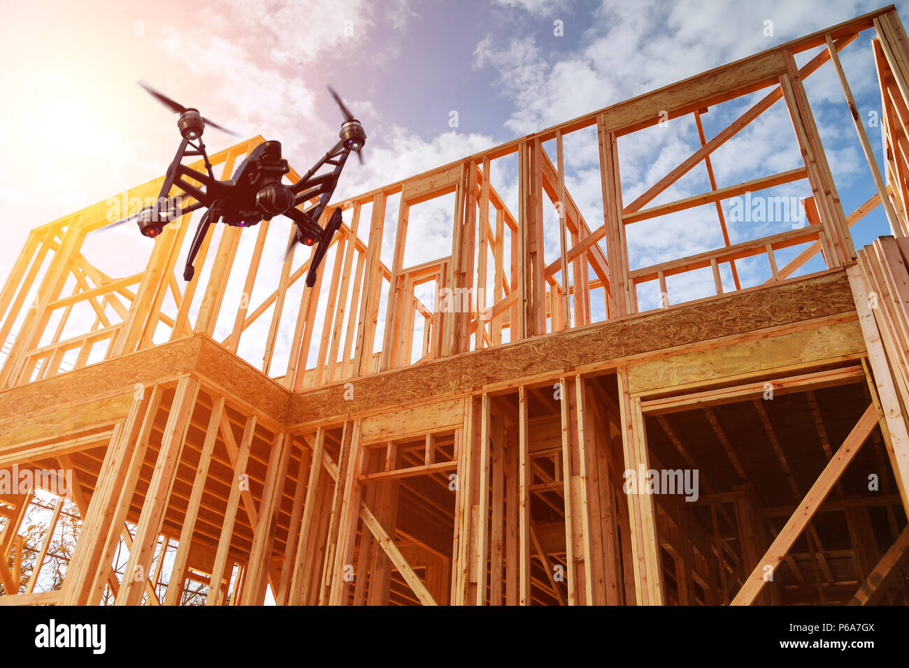 Black drone quadcopter with camera flying over residential construction home framing against a blue sky. Roofing construction. Wooden construction Stock Photo