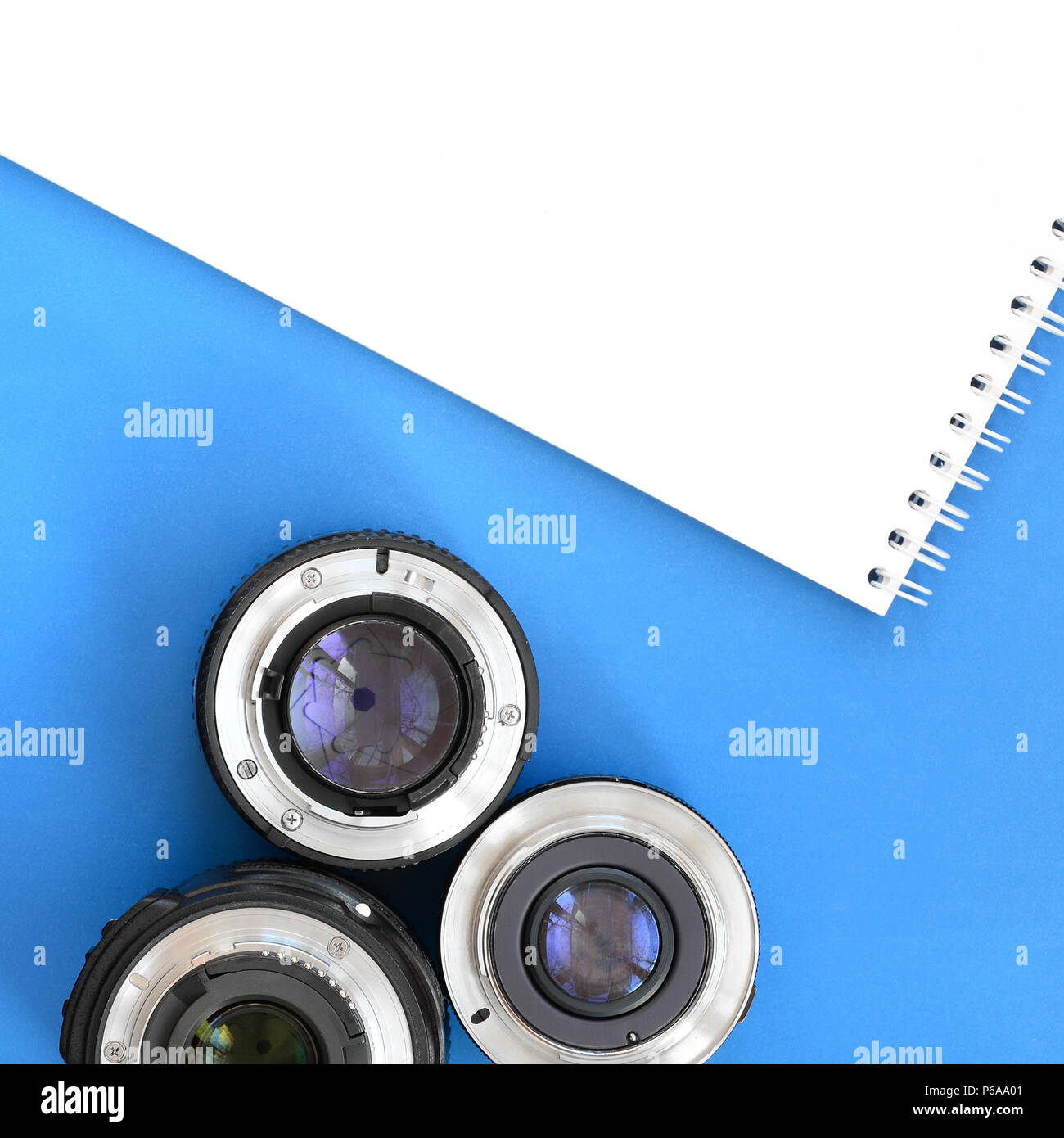 Several photographic lenses and white notebook lie on a bright blue ...