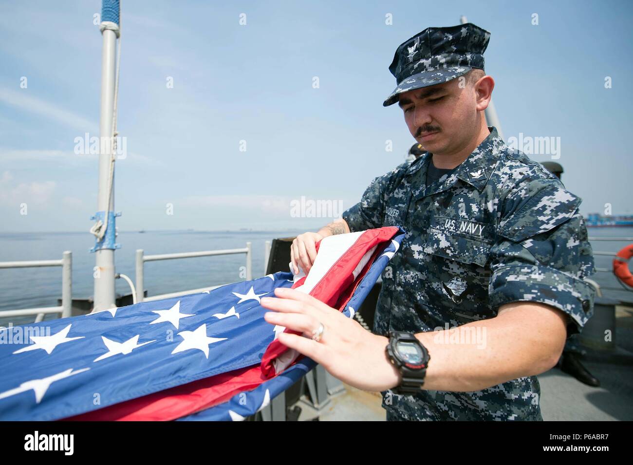 160528-N-EH218-063  MANILA, Philippines (May 28, 2016) – Electronics Technician 3rd Class Ryan Glover, from Lockhart, Texas, folds the national ensign after getting underway and shifting colors aboard the guided-missile cruiser USS Mobile Bay (CG 53). Providing a ready force supporting security and stability in the Indo-Asia-Pacific, Mobile Bay is operating as part of the John C. Stennis Strike Group and Great Green Fleet on a regularly scheduled 7th Fleet deployment. (U.S. Navy photo by Mass Communication Specialist 2nd Class Ryan J. Batchelder/Released) Stock Photo