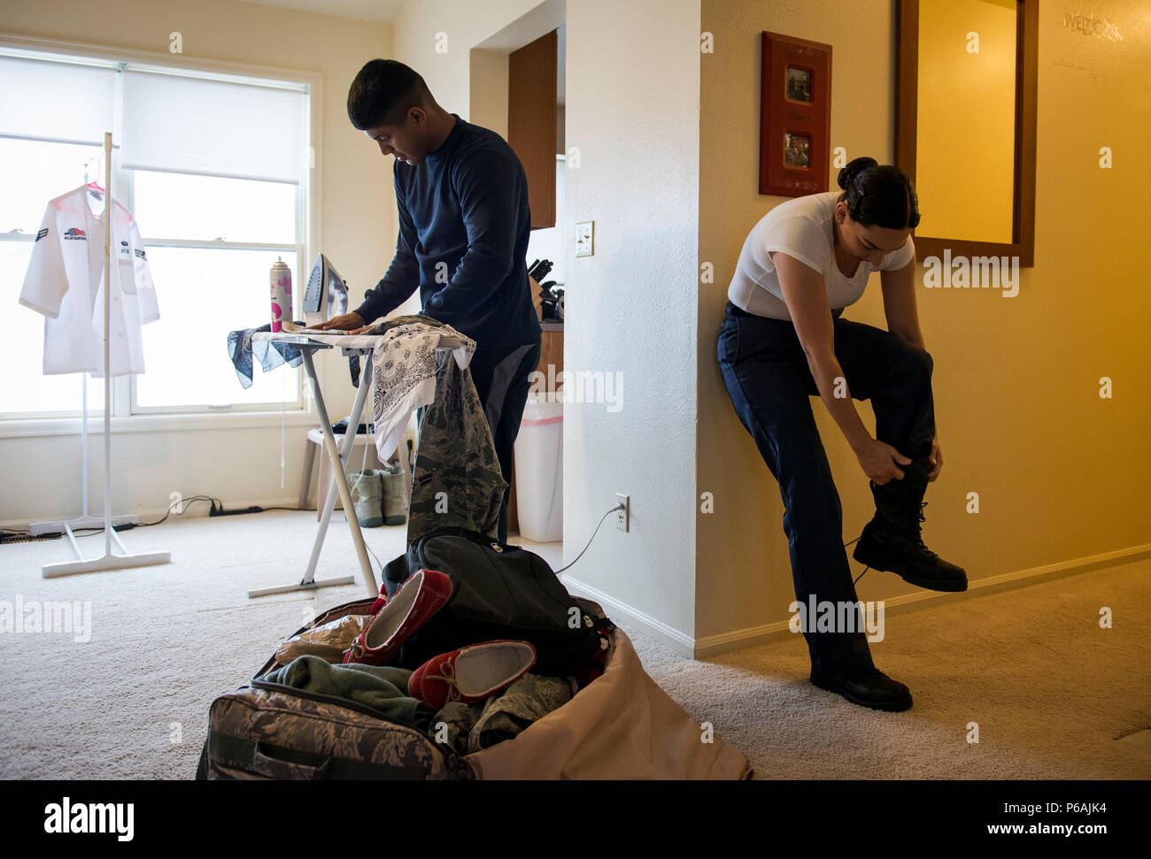 Airman 1st Class Ozzie Galvan (left) helps his wife, Airman 1st Class Alexandra Ayub, prepare for a four-day deployment by ironing and packing her clothes while she dresses at their home at Francis E. Warren Air Force Base, Wyoming. Ayub, a missile chef, regularly deploys to provide meals to the Airmen stationed at missile alert facilities that are many miles away from her home base. (U.S. Air Force photo/Staff Sgt. Andrew Lee) Stock Photo