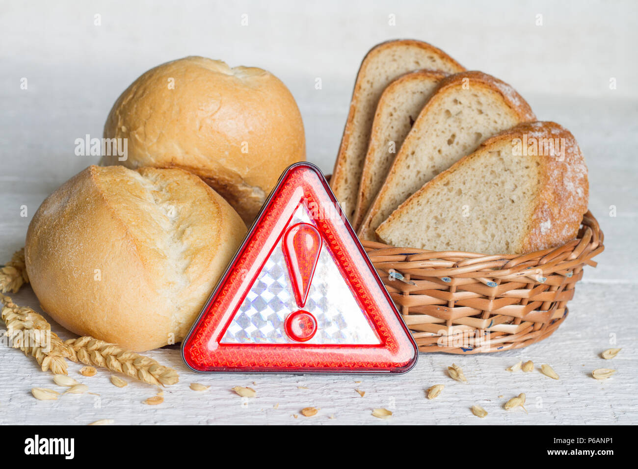 Gluten intolerance with bread wheat and warning sign on white planks