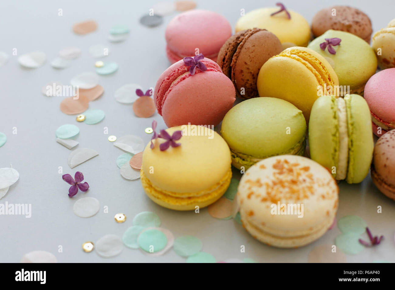 colorful macarons on trendy pastel gray paper with lilac flowers and confetti. tasty pink, yellow, green and brown macaroons. candy bar for party. foo Stock Photo
