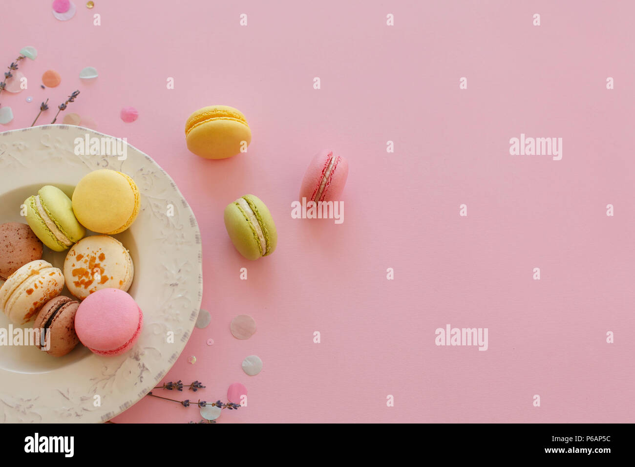 food photography flat lay of tasty colorful macarons in vintage plate on trendy pastel pink paper with lavender and confetti. space for text pink, yel Stock Photo