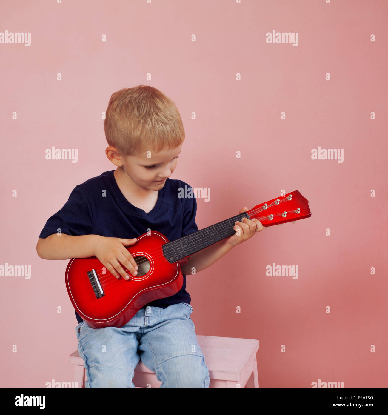 Little boy is learning to play on a small guitar. Study music. Ukulele.  Portrait on pink background Stock Photo - Alamy