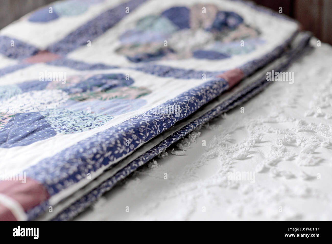 A folded quilt laying on top of a made bed and bedspread with shallow depth of field Stock Photo
