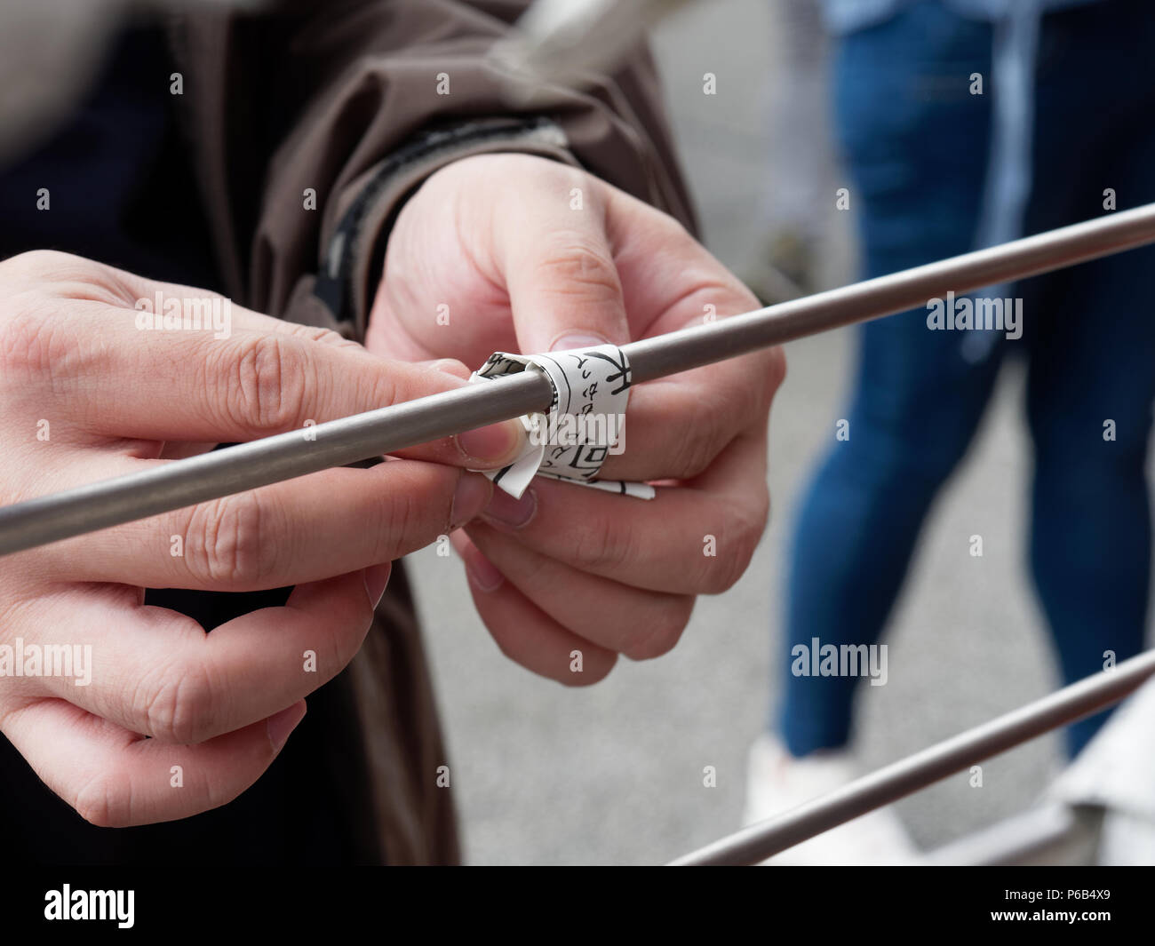 TOKYO, JAPAN - SEPTEMBER 28, 2017 : A tourist who select a bad fortune from Japanese fortune telling strip, Omikuji, tying his bad fortune paper with a pole to leave it at Sensoji temple, Asakusa Stock Photo