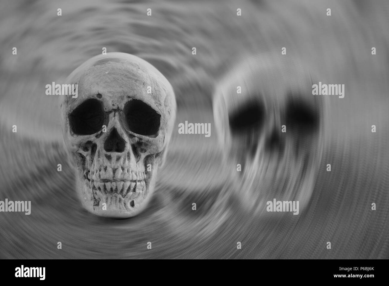 Bipolar disorder concept: two skulls on sand with one blurred in radial zoom Stock Photo