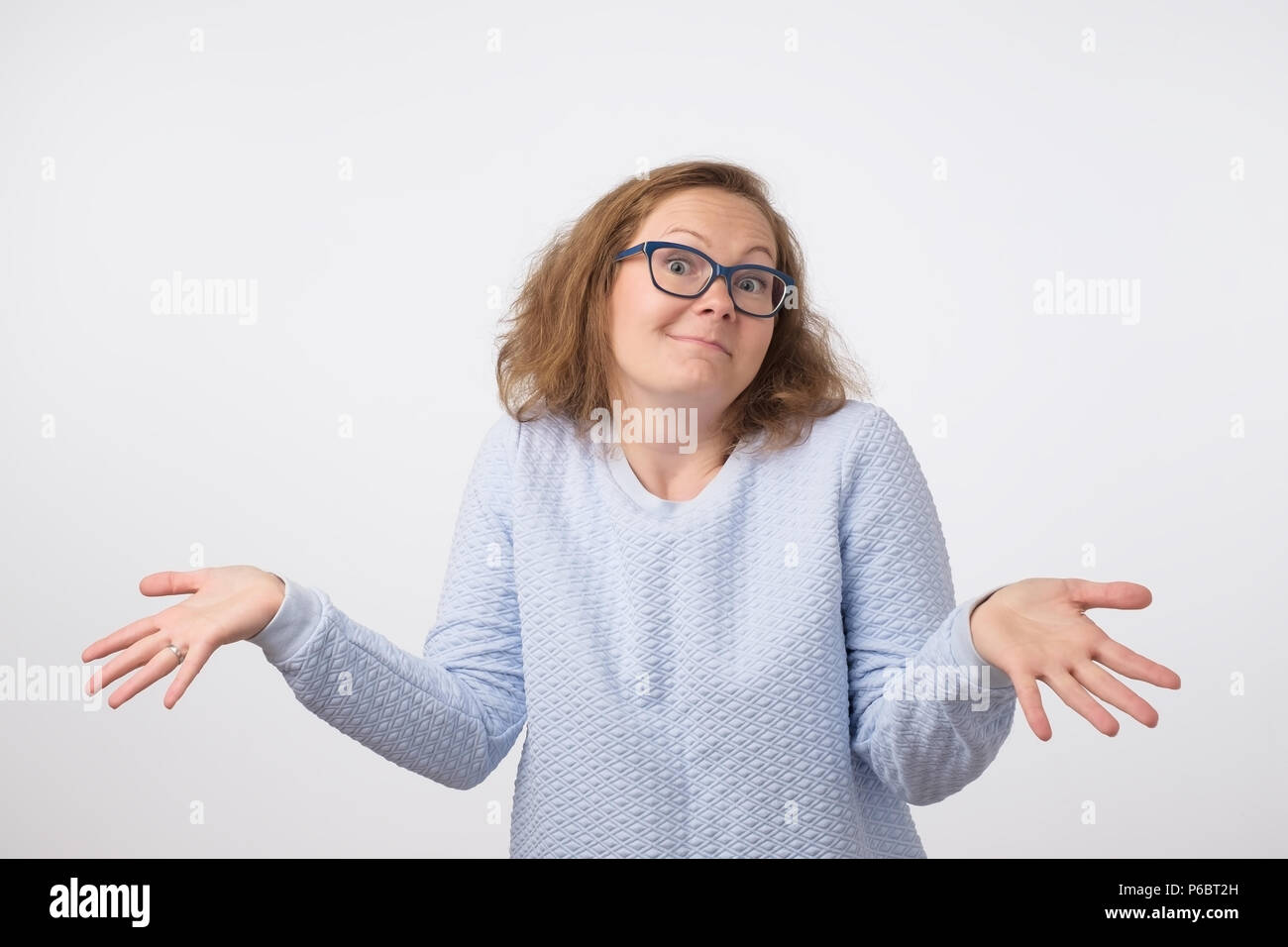 Shrugging norwegian woman wearing blue sweater in doubt doing shrug. Confused girl gesturing do not know sign on gray background Stock Photo