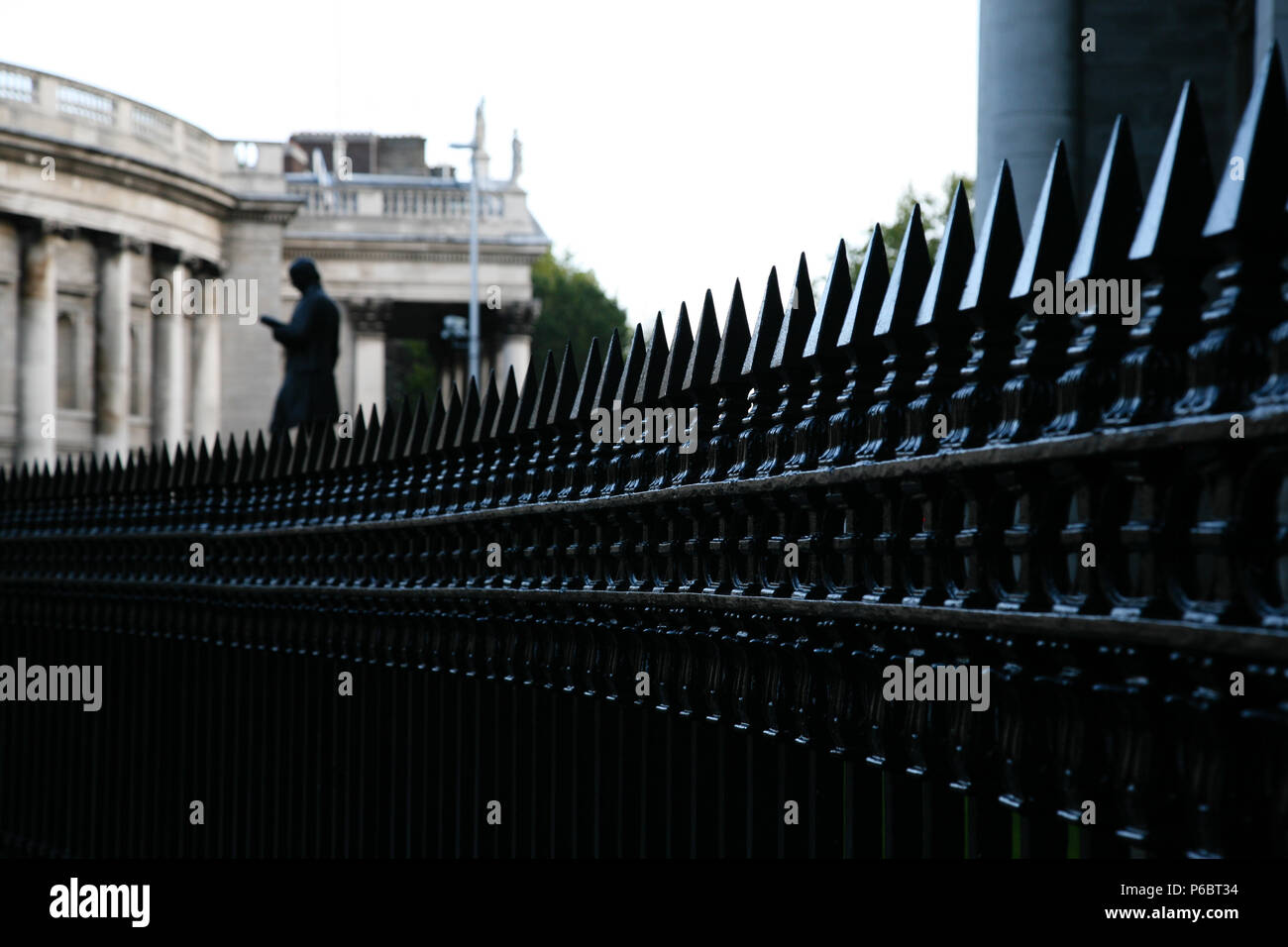 Black painted steel railing leading the eye towards an old city building with statue in the gardens, Dublin, Ireland. Stock Photo