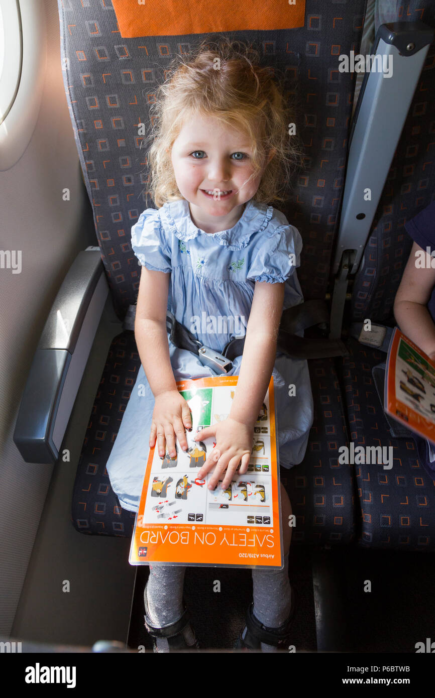 Child / girl aged 3 years old / three year old, reading safety instruction card while flying on an Airbus air plane / airplane / aeroplane flight (91) Stock Photo