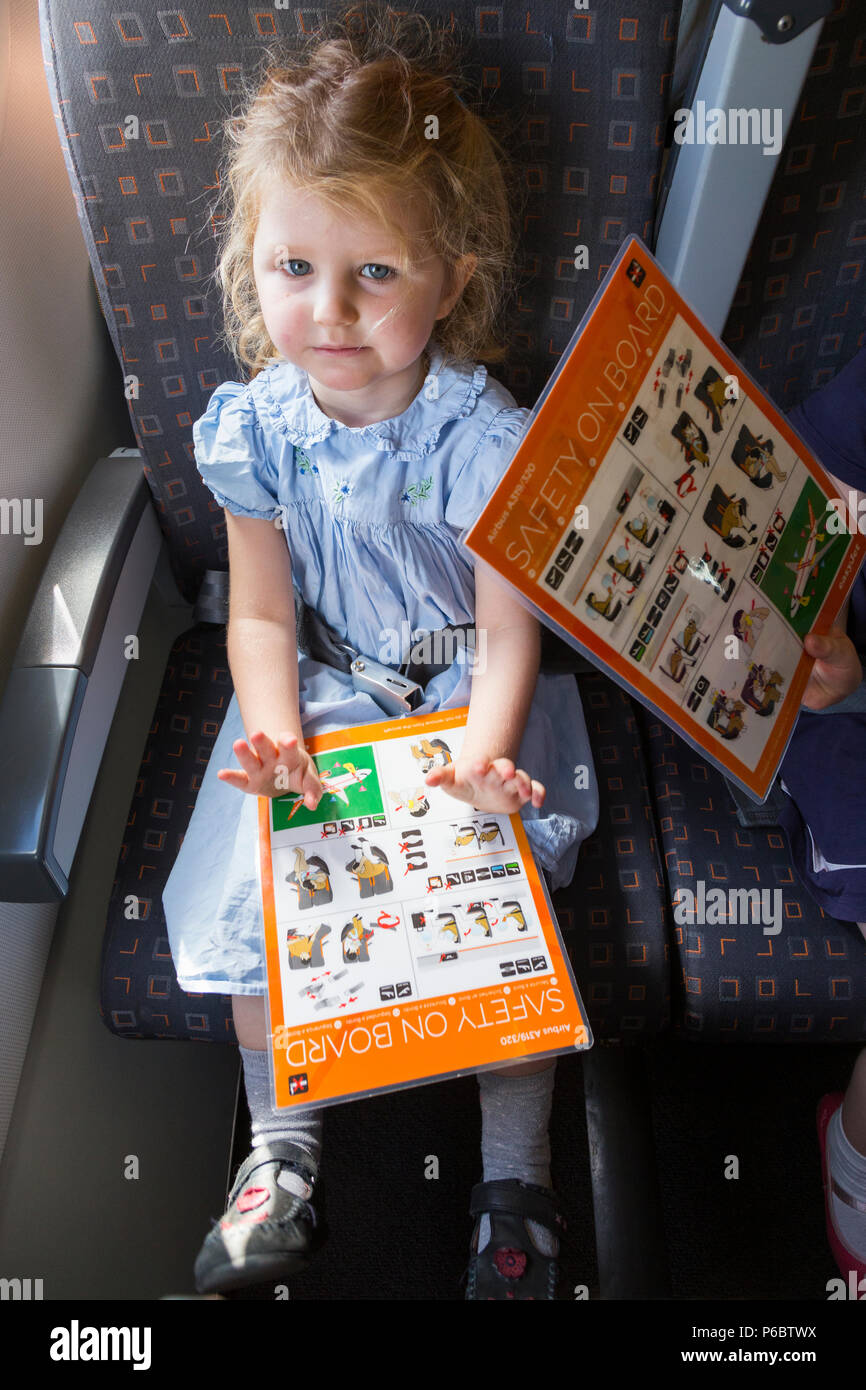 Child / girl aged 3 years old / three year old, reading safety instruction card while flying on an Airbus air plane / airplane / aeroplane flight (91) Stock Photo