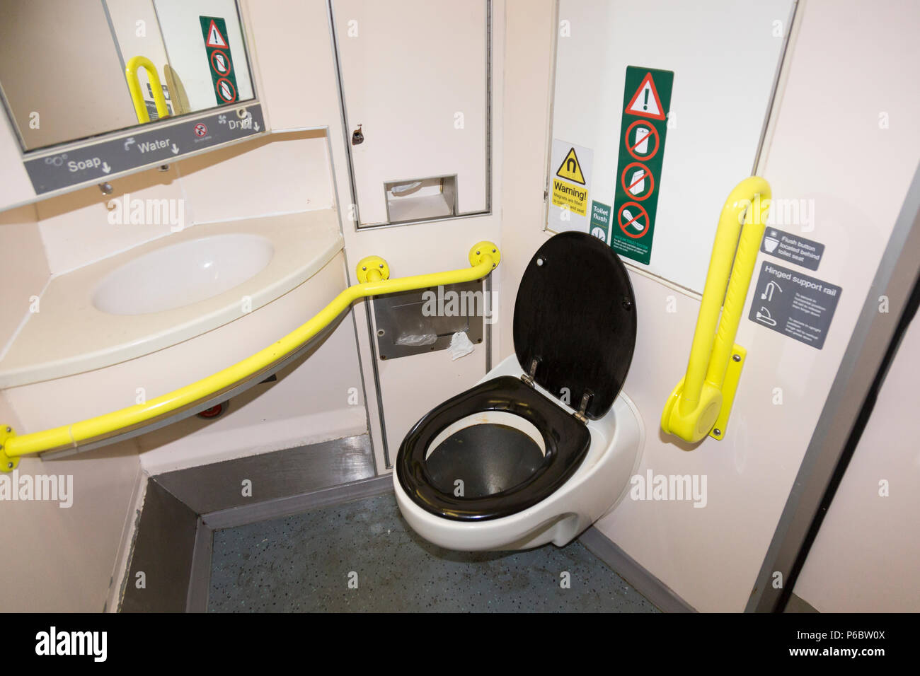 Railway toilet / lavatory – with wet floor and which is used & a little dirty – with disabled access and bars, & basin sink on UK train near SW London. UK. Stock Photo
