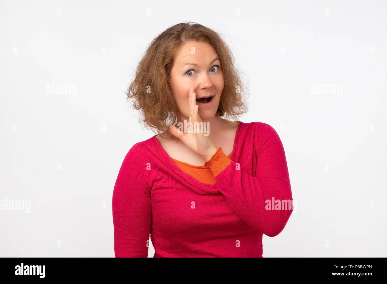 Do not tell anyone concept. Talkative woman in red sweater is saying secret news looking at camera. Gossip about other people's secrets Stock Photo
