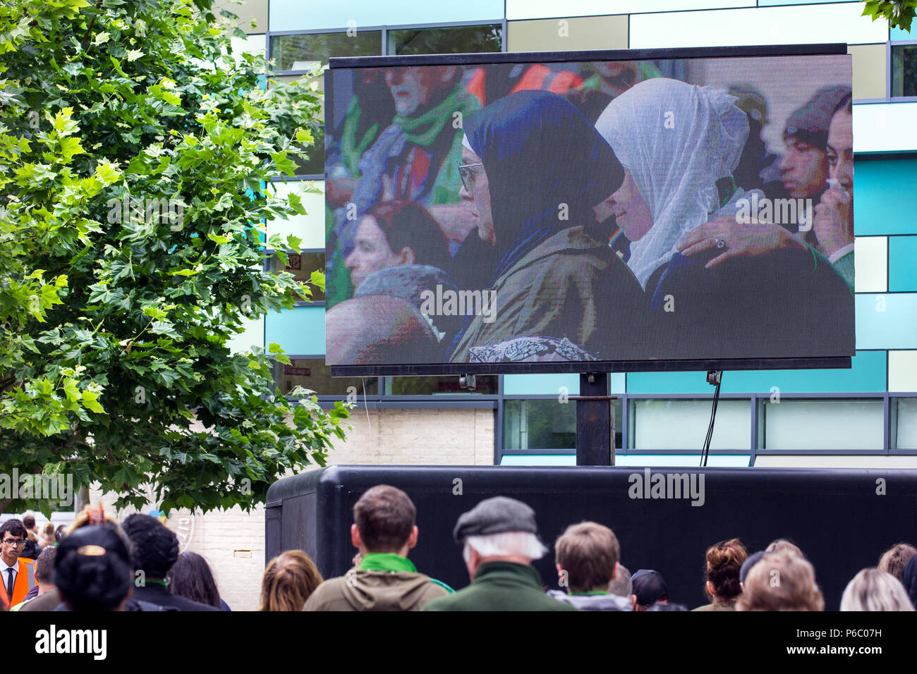 The first anniversary of the 24-storey Grenfell Tower block of public housing flats fire which claimed 72 lives. The outdoor TV screen televising the service.  South Kensington, London, UK, 14th June 2018. Stock Photo