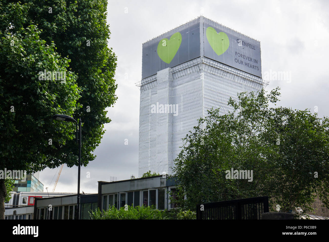 The first anniversary of the 24-storey Grenfell Tower block of public housing flats fire which claimed 72 lives. The burnt out shell has now been covered in a white tarpaulin with the message 'Grenfell Forever in Our Hearts' South Kensington, London, UK, 14th June 2018. Stock Photo