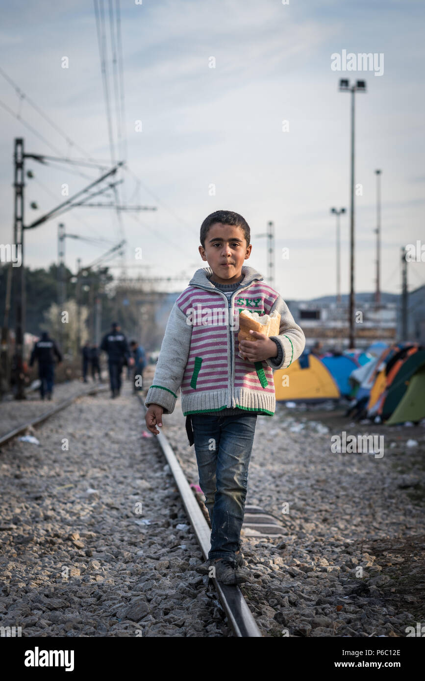 Refugee boy walks through the railway track with a bread in his hand at the train station of the Greek-Macedonian border near the Greek village of Ido Stock Photo