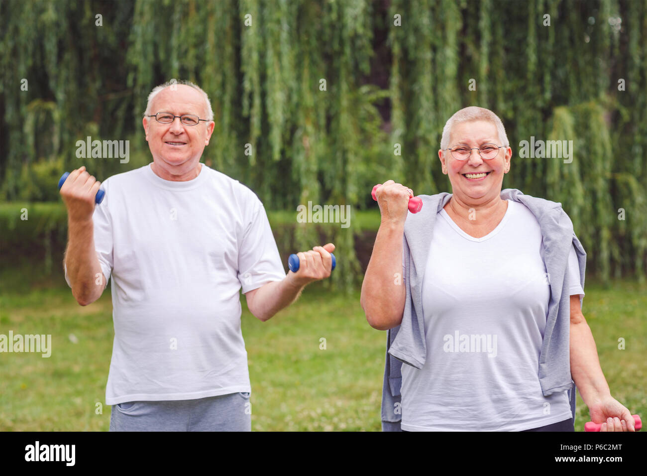 senior man and woman practice fitness exercise with dumbbells in a park at sunny day Stock Photo