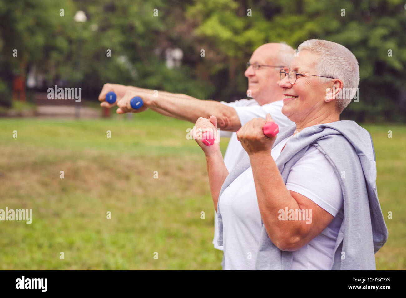 together we workout better - Smiling senior man and woman practice with dumbbells in a park Stock Photo