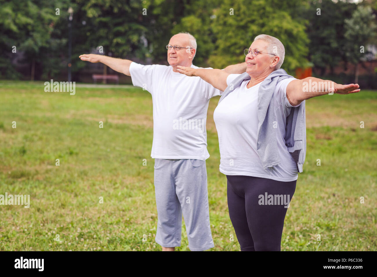 Smiling senior couple are outdoors in a park exercise with dumbbells and having fun together Stock Photo