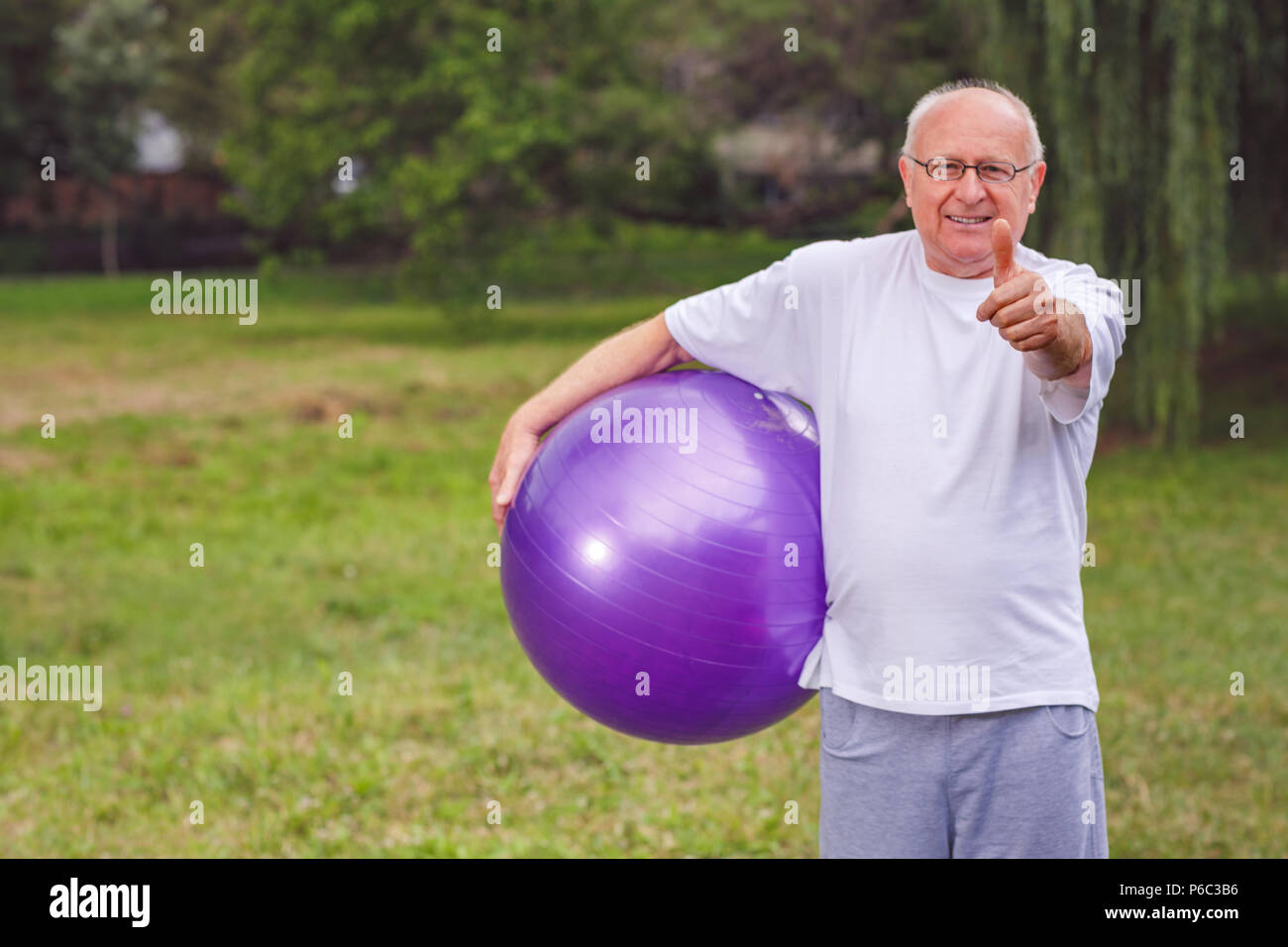 thumb up for healthy exercising - Happy senior man with fitness balls in park and exercising Stock Photo