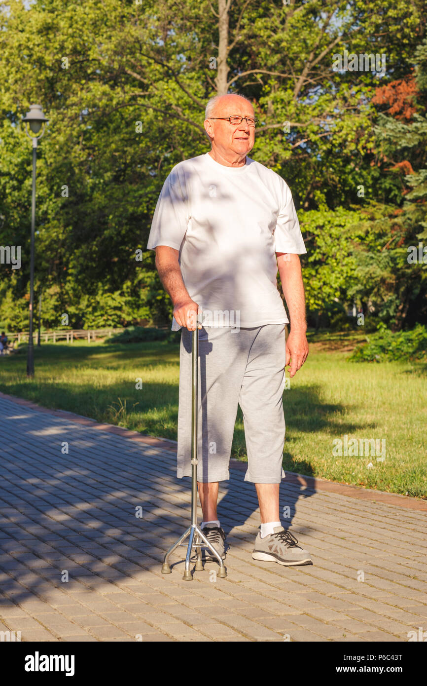 Smiling male pensioner enjoying walk in park with stick Stock Photo