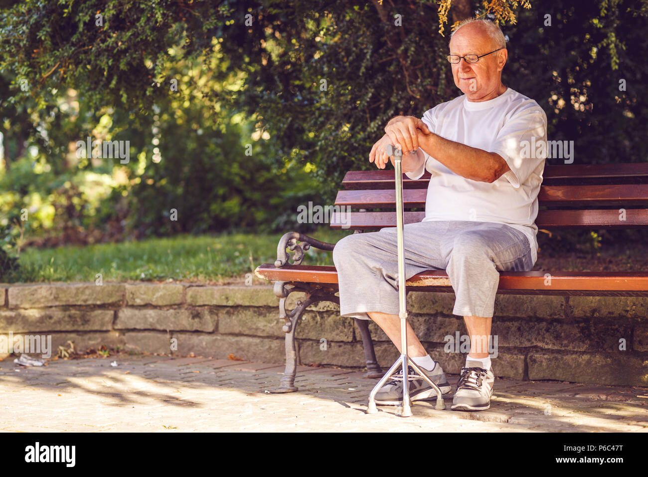 Sad elderly man with his walking stick sitting on bench in the park Stock Photo