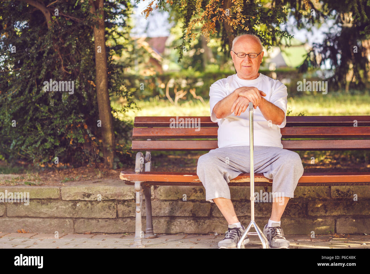 Alone elderly man with his walking stick sitting on bench in the park ...