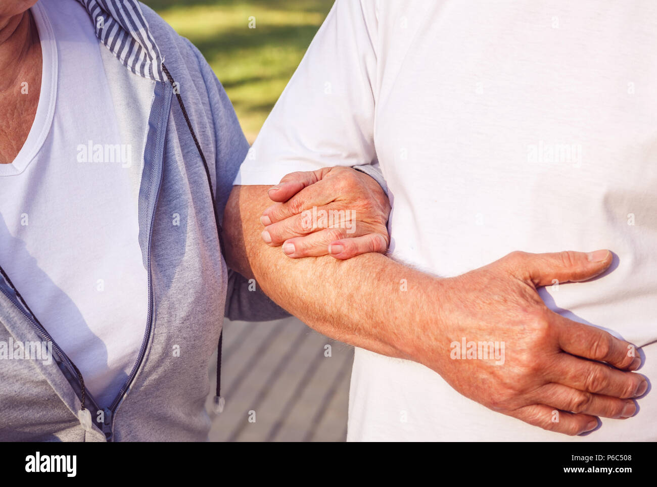 Close up of hands of romantic senior couple during walk in park on sunny day Stock Photo