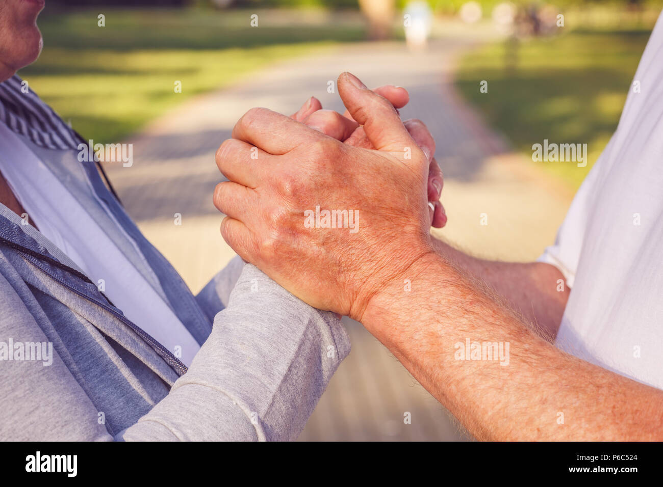 Close up hands of senior couple during walk in park on sunny day Stock Photo