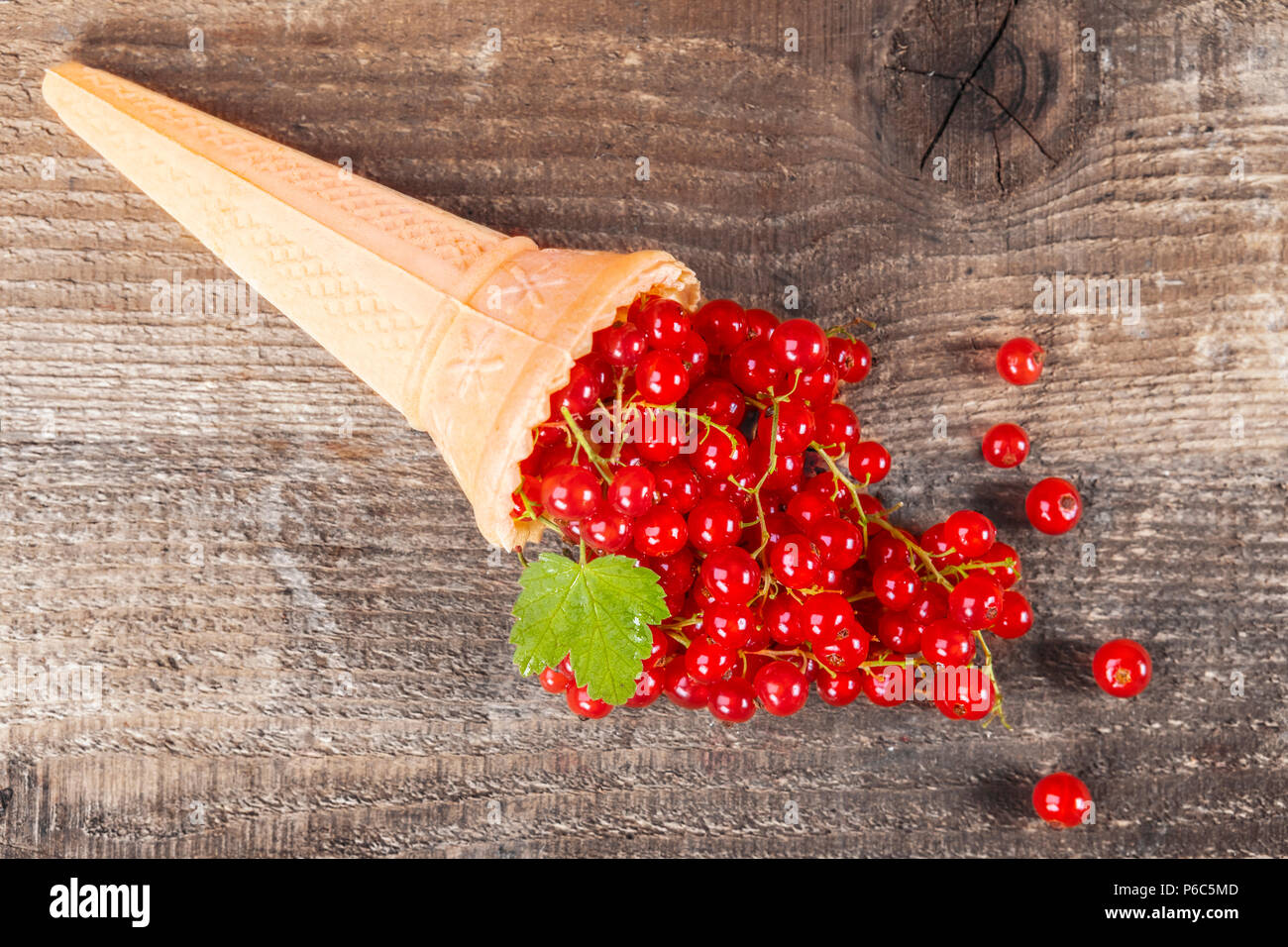 Red currant fruits in ice cream cone on wooden table. Focus on leaf. Stock Photo