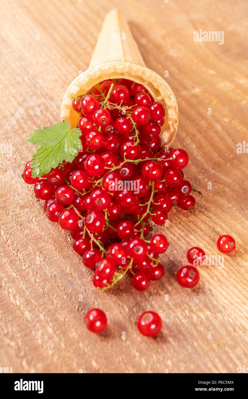 Red currant fruits in ice cream cone on wooden table. Focus on leaf. Stock Photo