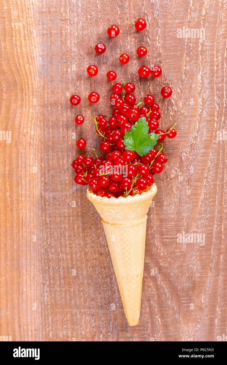 Red currant fruits in an ice cream cone on wooden table. Focus on leaf. Stock Photo