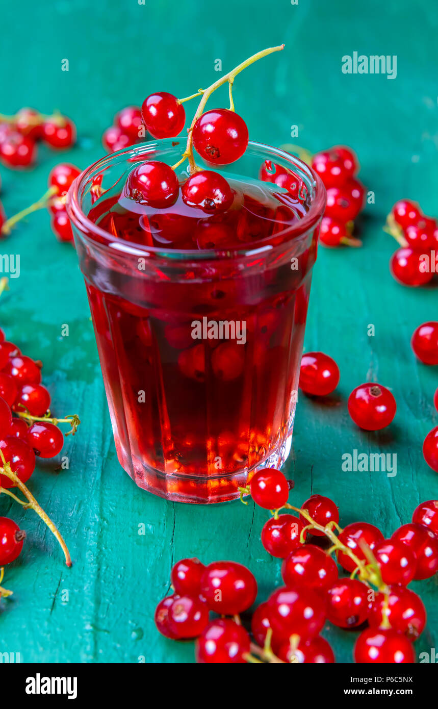 Red currant juice in glass with fruits on wood table. Focus on redcurrant in glass. Stock Photo