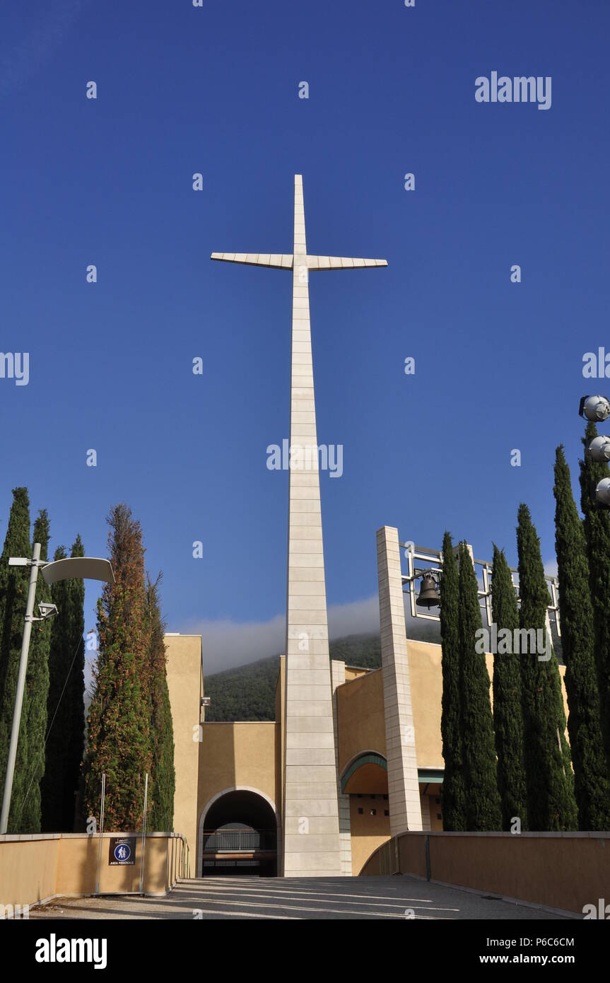 a cross at the end of a path with a building and a bell Stock Photo