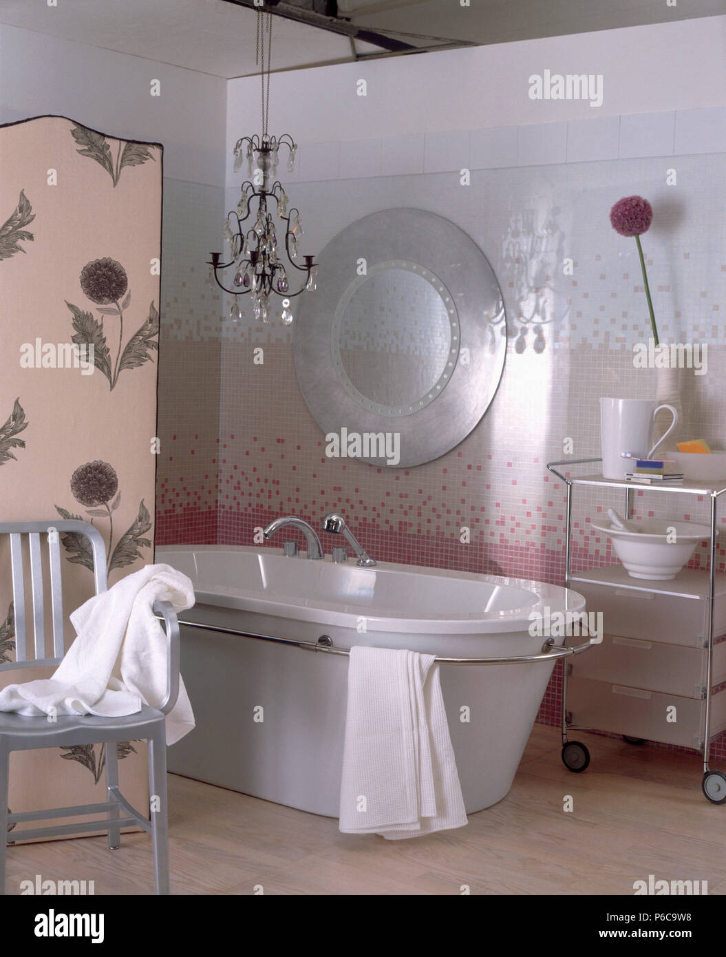 Simple chandelier and modern bath in bathroom with patterned pink screen and metal chair Stock Photo