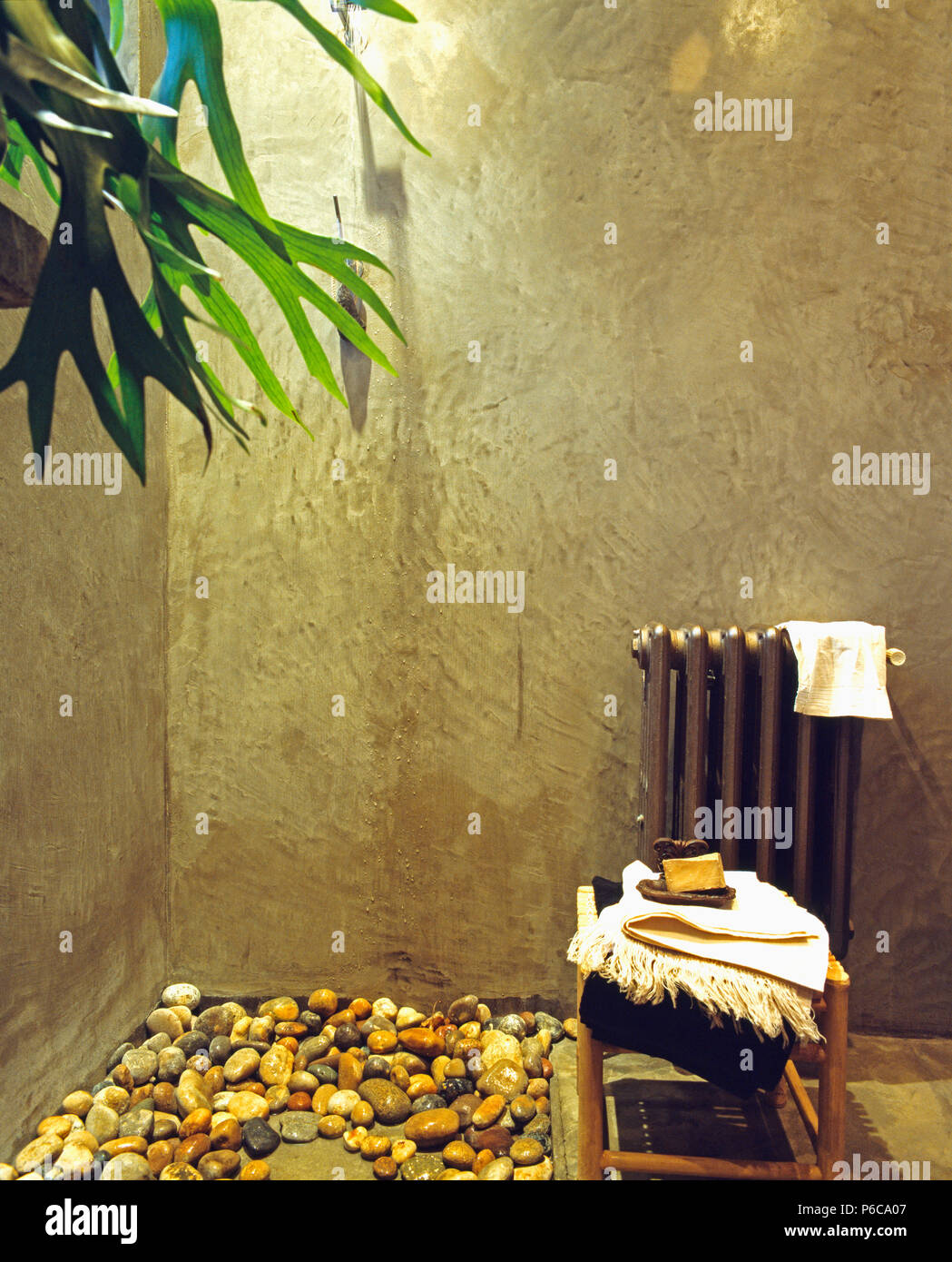 Concrete walls and pebbles on floor of shower with towels beside vintage radiator Stock Photo