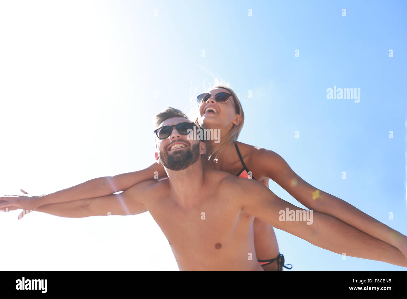 Man carrying woman piggyback on beach. Stock Photo