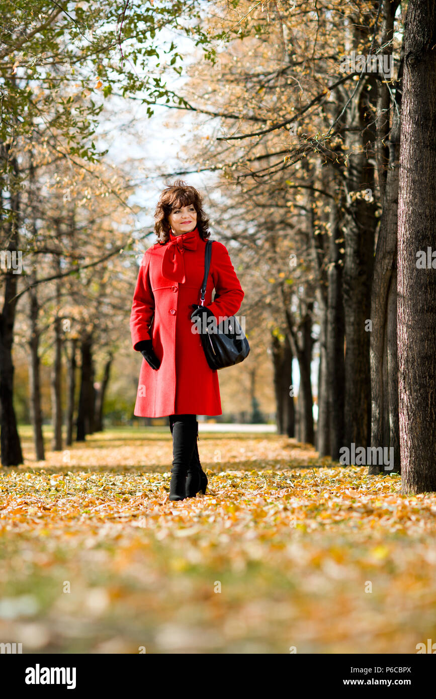 The  mature beautiful woman in red topcoat,  outdoor in park, autumnal day Stock Photo